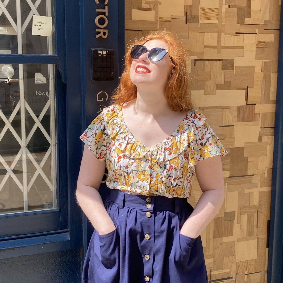 Woman modelling Charleston floral top with blue button skirt and sunglasses
