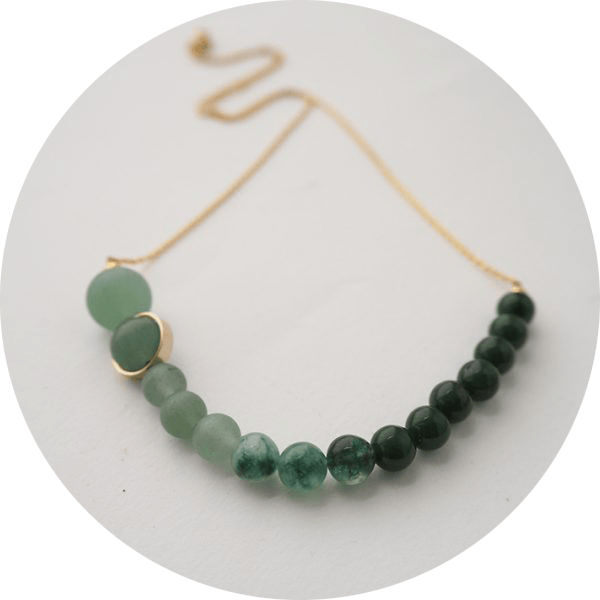 A necklace made up of labradorite, aventurine and amazonite beads in varying shade of green on a brass chain,.