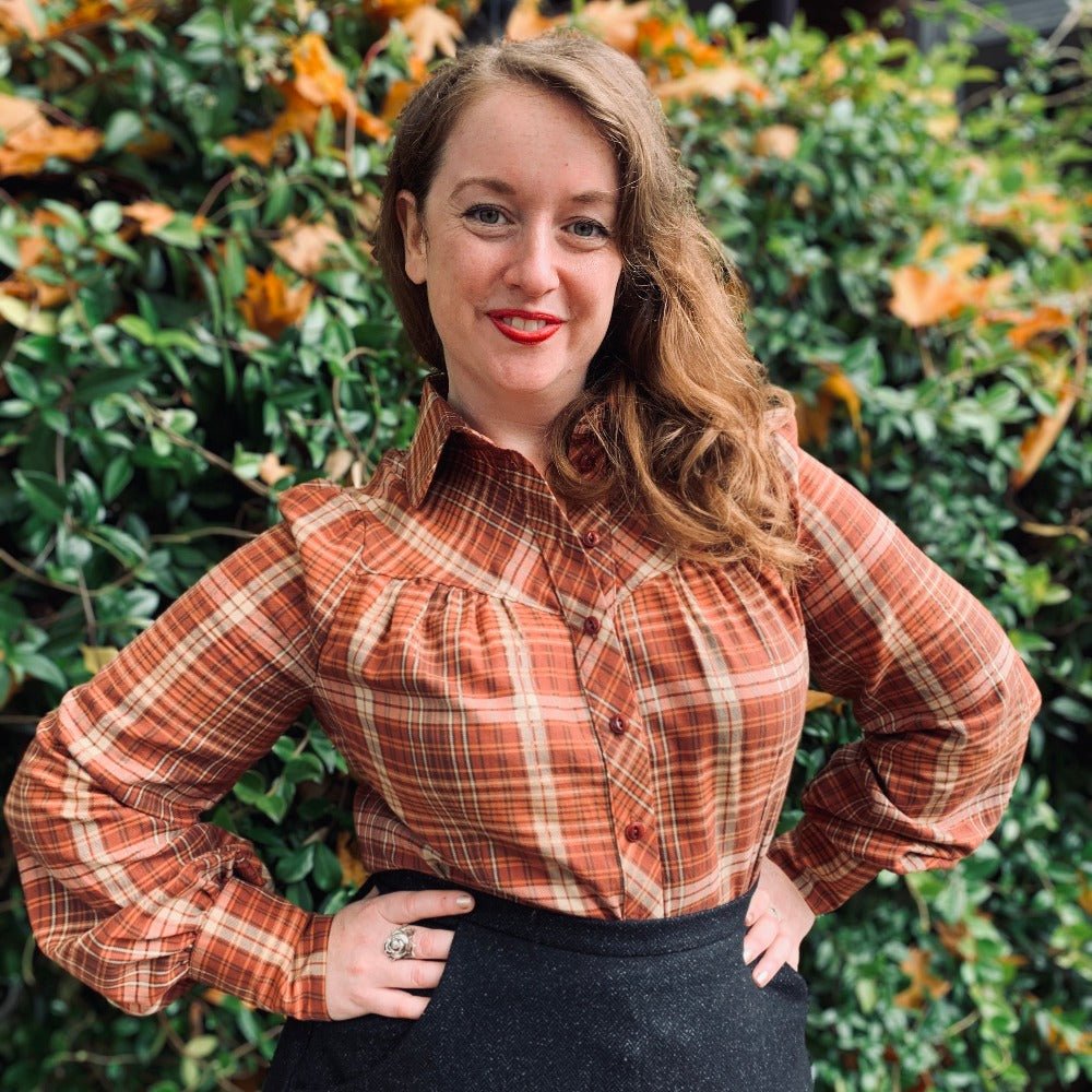 Vintage inspired blouse with long sleeves and round collar- The Bishopess Blouse by Emmy Design Sweden in rust plaid as worn by Mary who faces the camera with hands on hips.