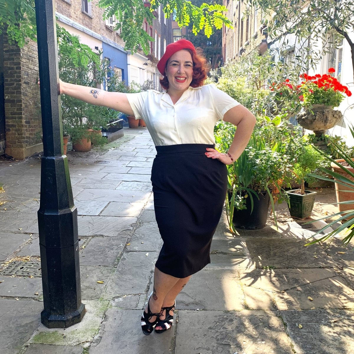 Smiling burlesque performer wears vintage inspired black pencil skirt with a cream white 1940s  style blouse tucked in.