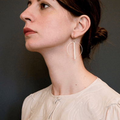 A white model side on wears Deco inspired brass circle earrings