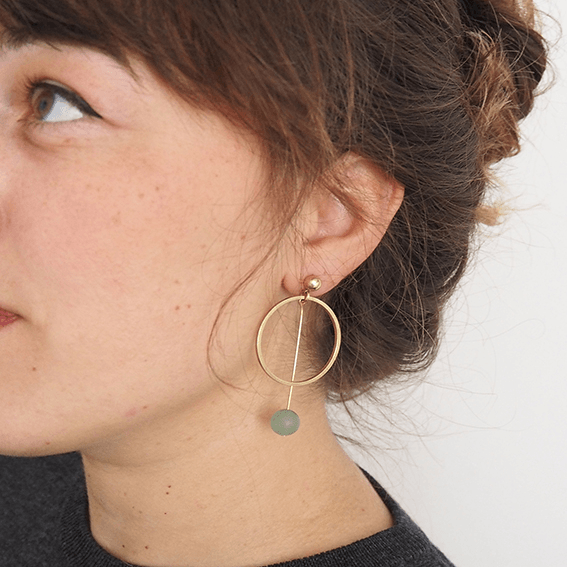 A close up of a brass earring made up of a circle and a long drop with an aventurine ball on the end