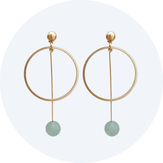 A close up of a brass earring made up of a circle and a long drop with an aventurine ball on the end