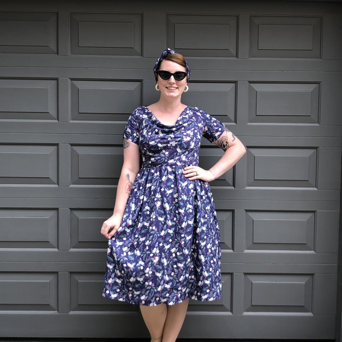 Vintage style dress in a 1950s silhouette in a bramble print as worn by Lottie who is standing with one hand on her hip as she smiles straight to the camera.