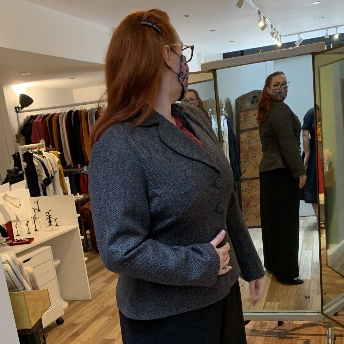 Pure wool jacket in a stone colour worn by a redhead who stands side on in front of a mirror where you can see her whole outfit  is vintage inspired
