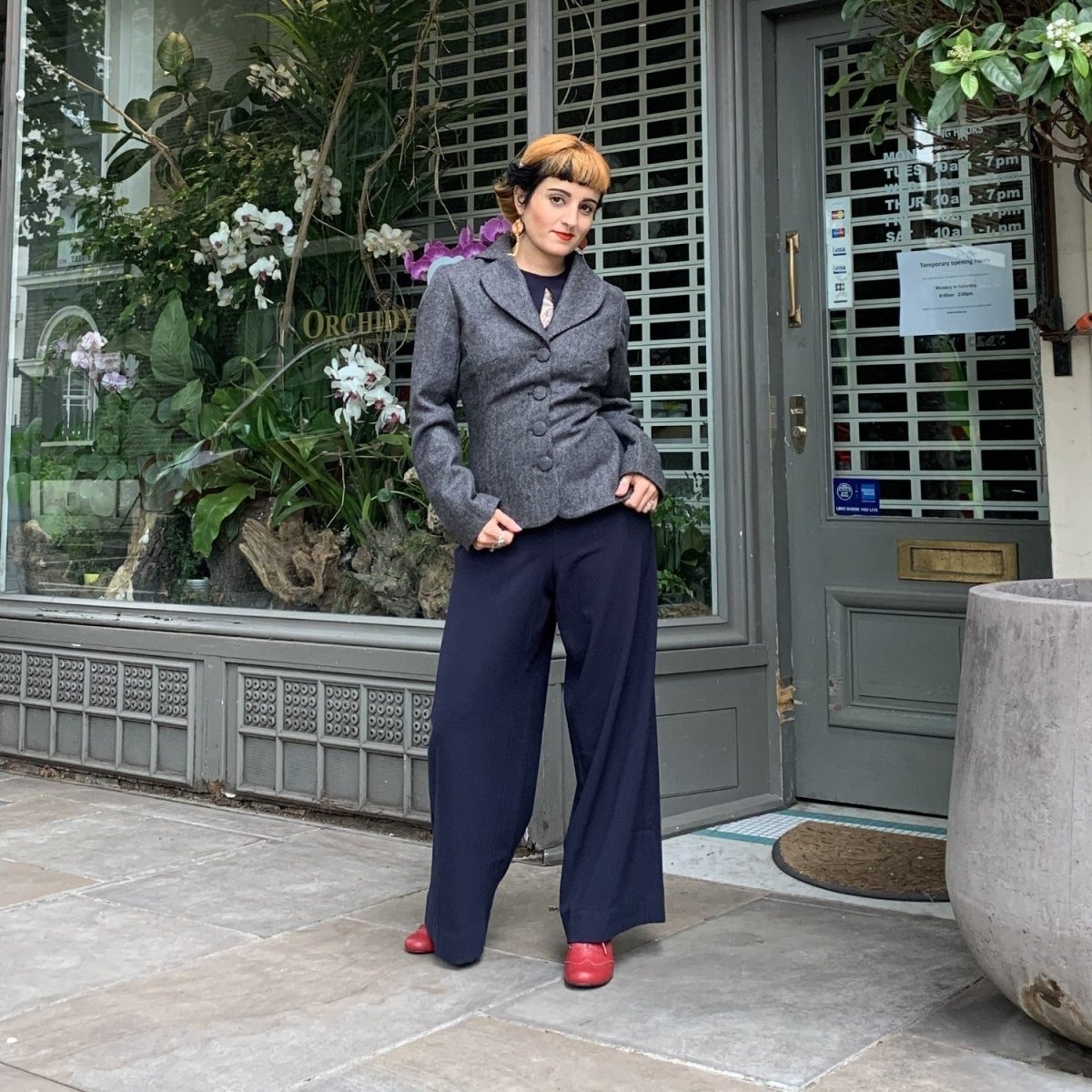 Pure wool jacket in a stone colour worn over a navy jumpsuit by Sara who stands in front of a florist shop.