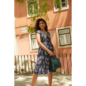 Wrap dress in vintage floral made in Britain by Revival Retro and worn by a woman of colour with shoulder length curly hair who is looking to the side and smiling